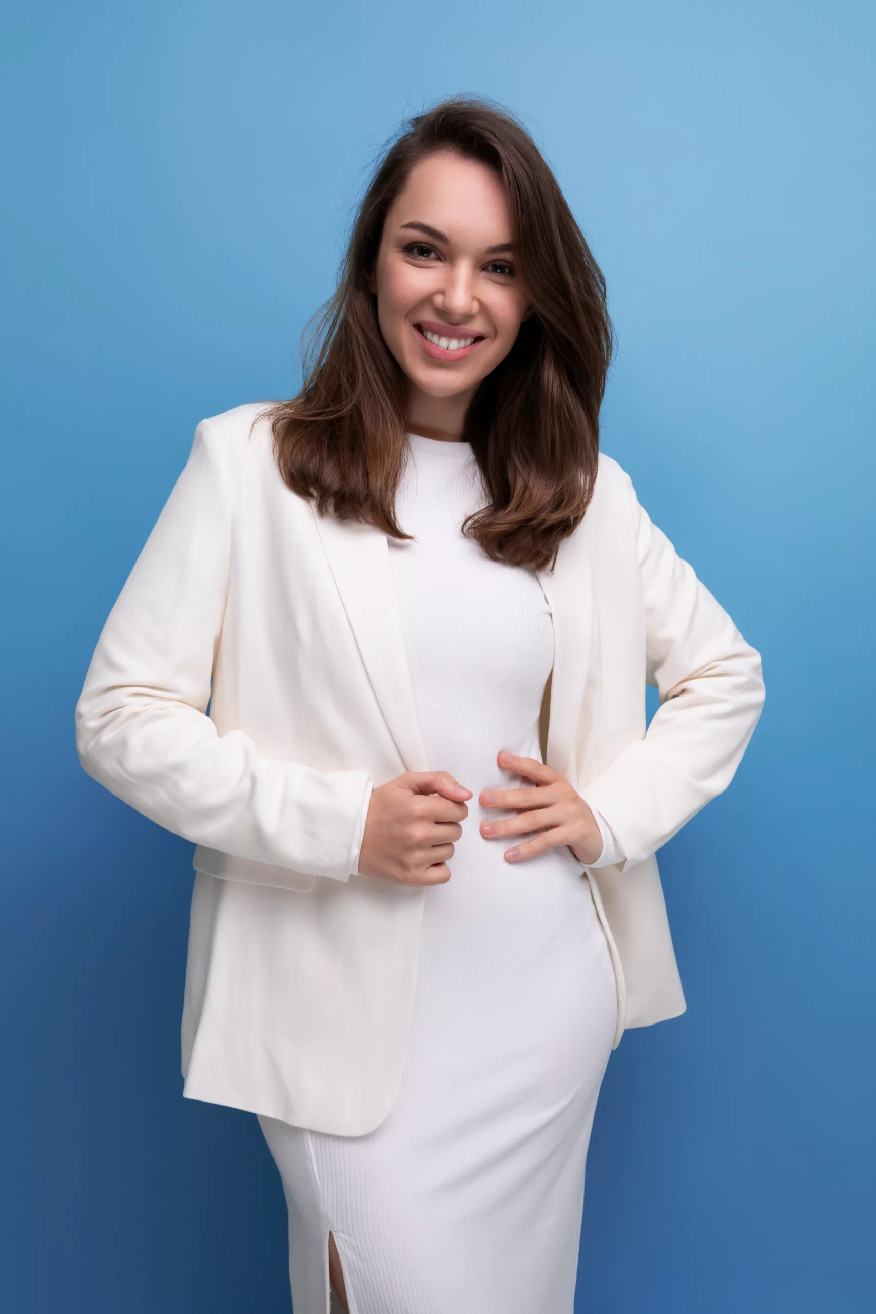 Stylish young brunette woman in white dress shows her confidence and smile